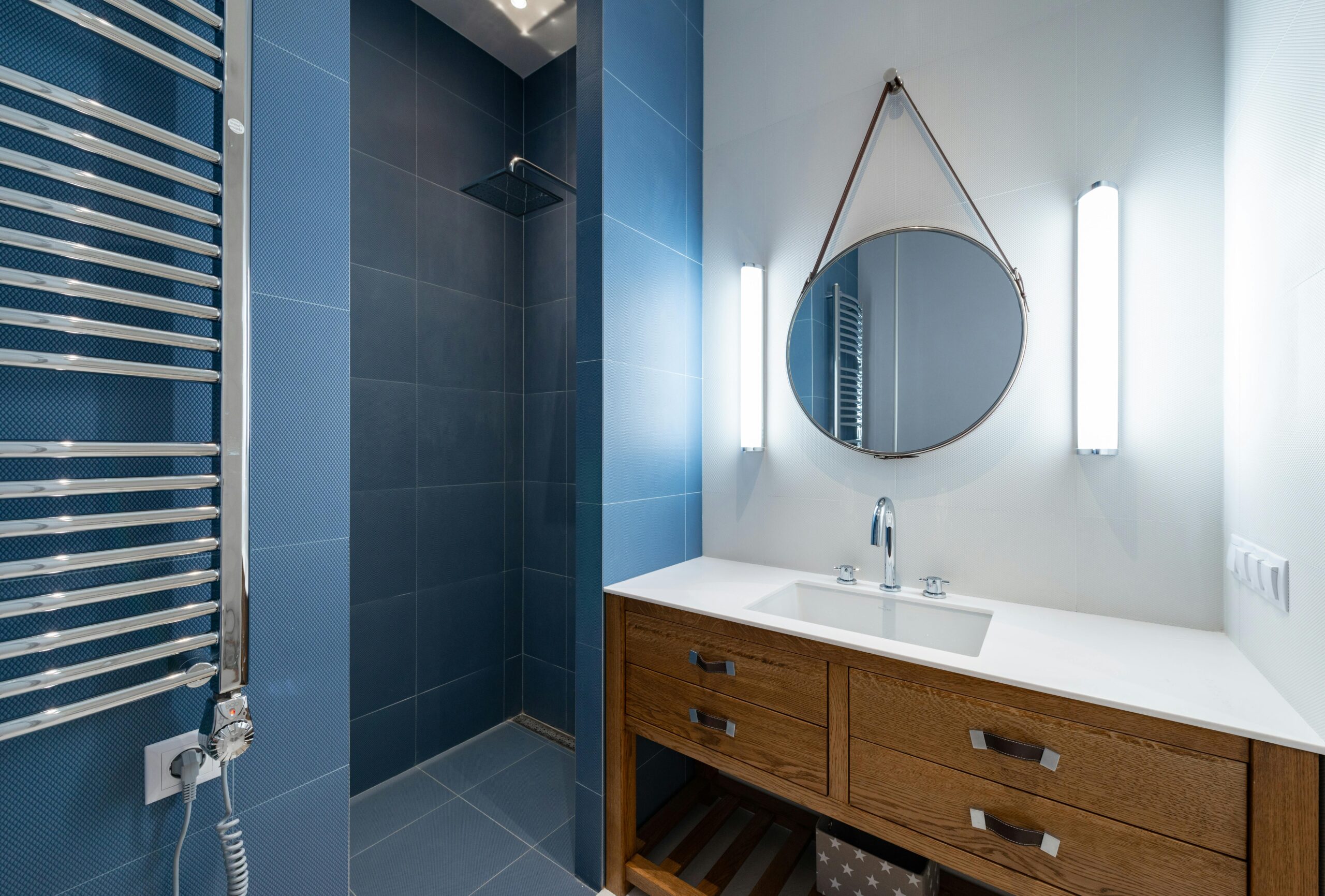 Interior of stylish bathroom with blue tile in shower and round mirror hanging on wall above sink