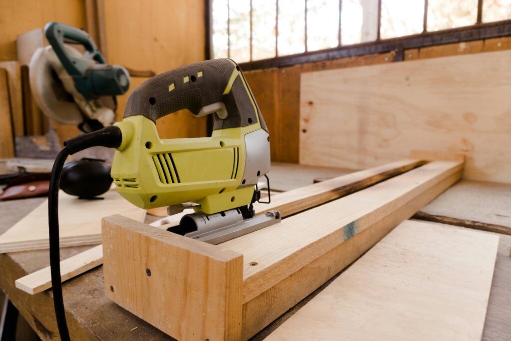 A close-up of an electric jigsaw placed on a wooden workbench in a carpentry workshop.